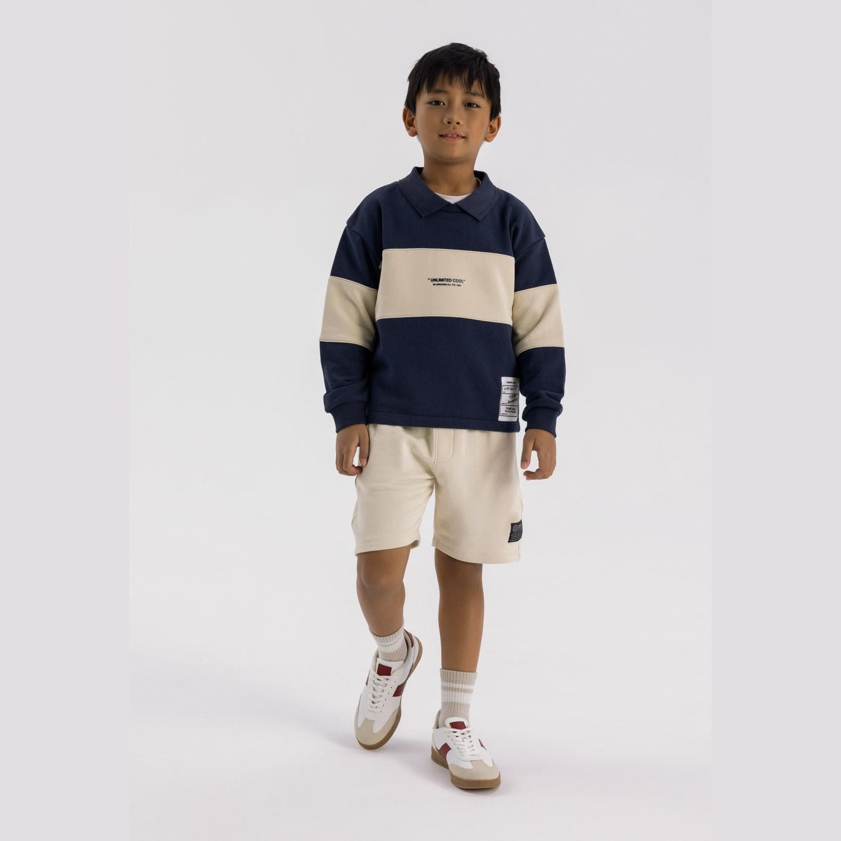 Boy wearing navy fleece jumper with cream contrast panels and matching cream shorts, full body front view on white background