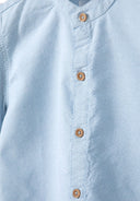 Detail of a boys grandad shirt in light blue with button fastening and stand-up collar.