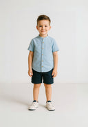 Boys grandad shirt in light blue with button fastening and navy shorts, front view.