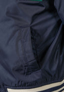 Close-up of boys navy padded varsity bomber jacket showing side pocket and ribbed hem.
