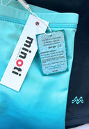 Close-up of boys swim shorts with Minoti brand tags highlighting UPF 50+ fabric protection and breathable quick-dry design