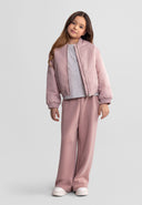 Young girl wearing a stylish lightweight pink bomber jacket with relaxed matching pants against a neutral background