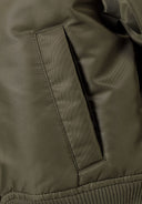 Detail of a khaki bomber jacket showing a side pocket and quilted fabric.