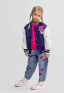 Girl wearing a navy and white varsity bomber jacket with patch details and casual embroidered jeans in kids fashion style