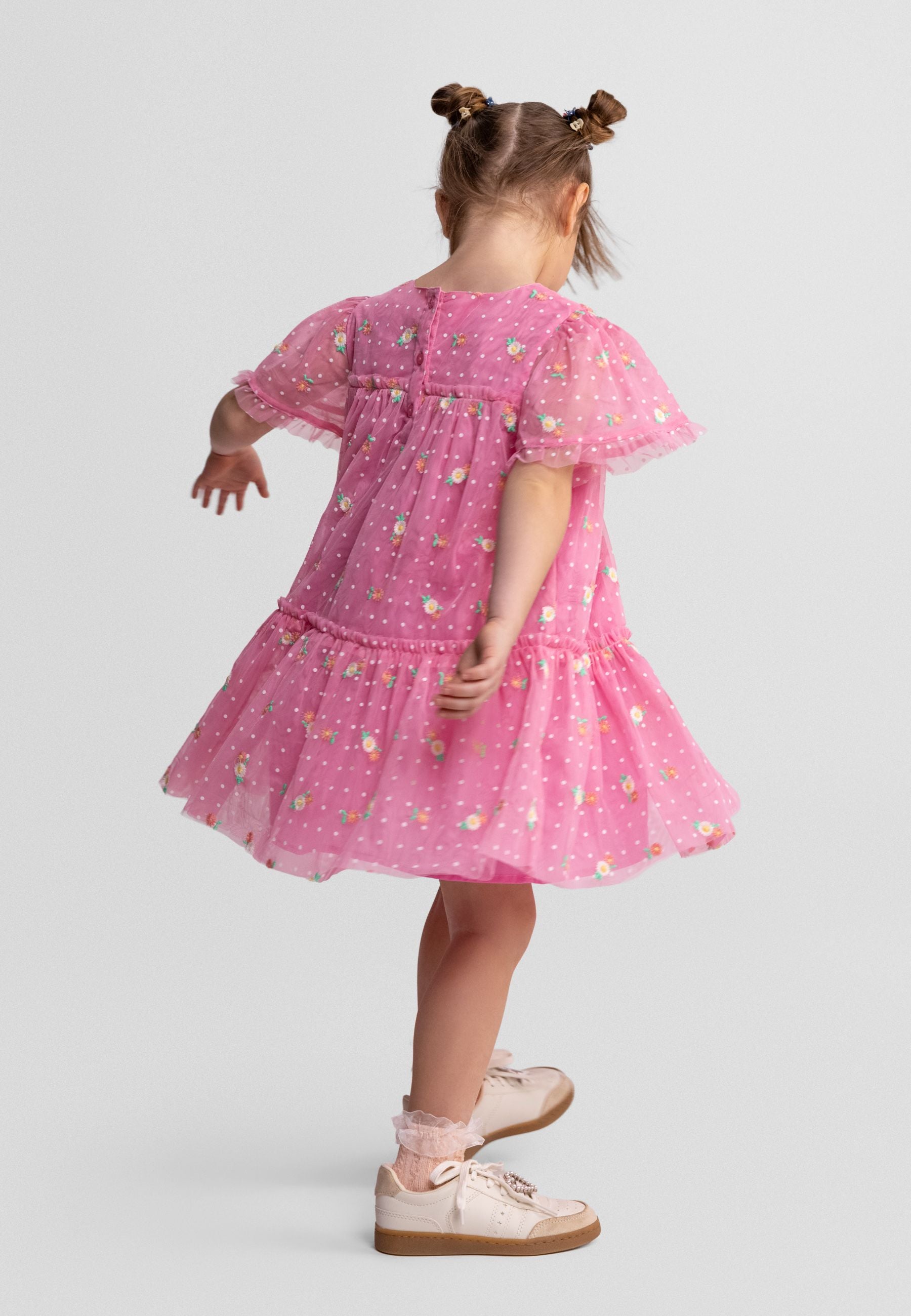 Back view of pink tulle dress showing button closure, floral embroidery details and tiered construction on white background