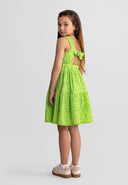 Young girl wearing sleeveless tiered dress with floral pattern and adjustable bow tie at back, standing sideways.