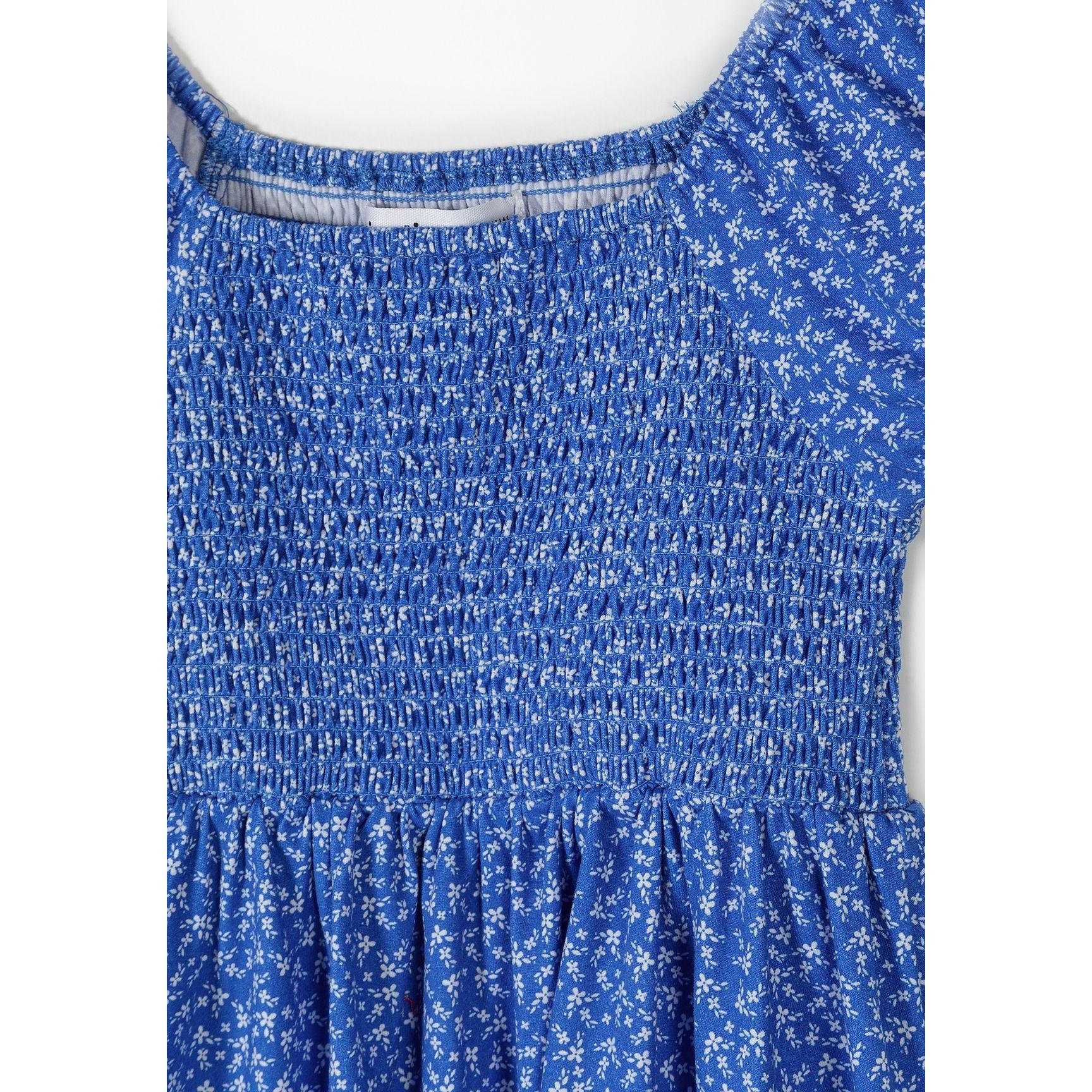 Close-up detail of blue floral dress showing shirred elasticated bodice texture and small white flower print pattern on blue fabric