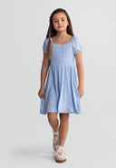 Young girl wearing a light blue floral dress with short sleeves and square neck, walking confidently in casual shoes