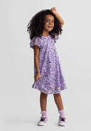 Smiling young girl wearing a multicolour sequin dress with flared sleeves and casual sneakers.