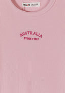 Close-up of pink ribbed fabric with embroidered "AUSTRALIA SYDNEY 1987" text on girls' dress design.