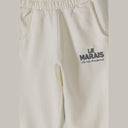 Close-up of off-white girls' joggers with "LE MARAIS" print, elasticated waist, and side pockets.