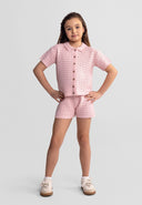 Young girl wearing soft pink pointelle knit short set with button-up top and shorts, showcasing delicate design and kids fashion.
