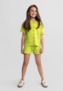 Smiling girl wearing a bright green pointelle knit shorts set with button-up top and white sneakers, showing unique design.