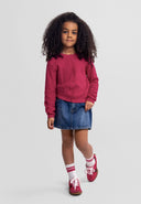 Young girl wearing a slim fit pink cardigan with buttons, paired with a denim skirt and casual sneakers in kids fashion style.