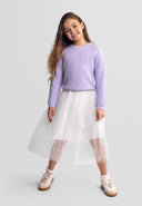 Young girl wearing a lilac jumper with waved trim and a white tulle skirt smiling confidently in kids fashion style