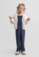 Young girl wearing a white cotton knit cardigan with button-up design, styled with a navy blue patterned jumpsuit.