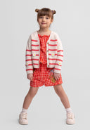 Young girl wearing a coral and white striped cardigan with daisy embroidery, paired with a red checkered outfit.