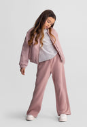 Young girl wearing pink wide leg joggers and matching jacket in a relaxed kids fashion pose with casual style design.