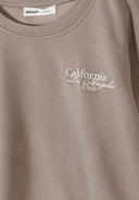 Close-up of brown sweatshirt with round neckline and white embroidered California Los Angeles Club design.