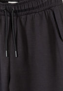 Close-up of black wide leg joggers with elasticated waistband and drawstring detail showing smooth fabric texture.