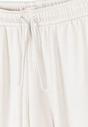 Close-up of off white wide leg joggers with elasticated waistband and drawstring detail showing soft viscose fabric texture.