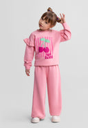 Young girl wearing a pink cotton blend tracksuit with cherry design and ruffle detail on the sleeves