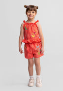 Young girl wearing red gingham shorts set with colorful fruit embroidery and ruffle details, smiling confidently