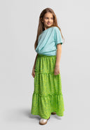 Young girl wearing green floral maxi skirt with elasticated waist and casual light blue top, smiling confidently.