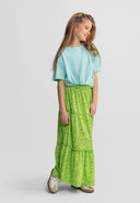 Young girl wearing a green floral maxi skirt with elasticated waist paired with a casual light blue top, smiling sideways.