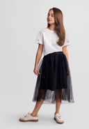Young girl wearing a black pleated tulle skirt paired with a white embellished t-shirt and casual sneakers