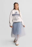 Young girl wearing a grey pleated tulle maxi skirt with a casual white sweatshirt and sneakers, smiling confidently.