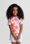 young girl wearing a short sleeve multicolour rash top with vibrant tie-dye design and casual white shorts