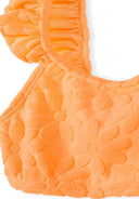 Close-up of orange textured fabric with raised floral pattern and ruffle trim design on kidswear.