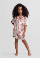 young girl wearing cream and pink short sleeve pyjama set with strawberry design standing confidently