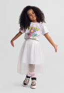 Young girl wearing a short-sleeved t-shirt with colorful flower design and a white tulle skirt, smiling confidently.