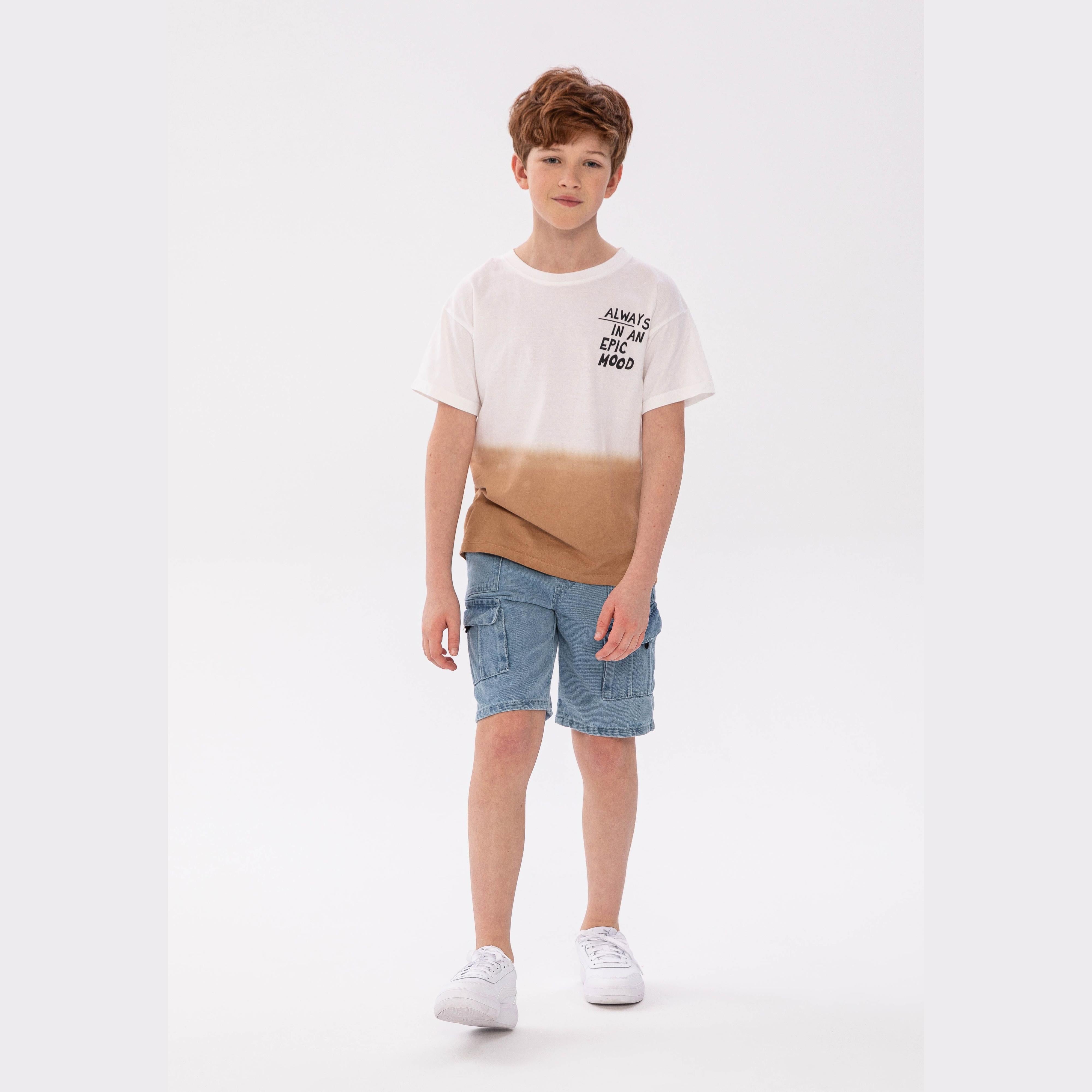 Boy wearing white dip dye t-shirt with brown gradient and 'Always In An Epic Mood' puff print, paired with denim shorts and white sneakers on white background