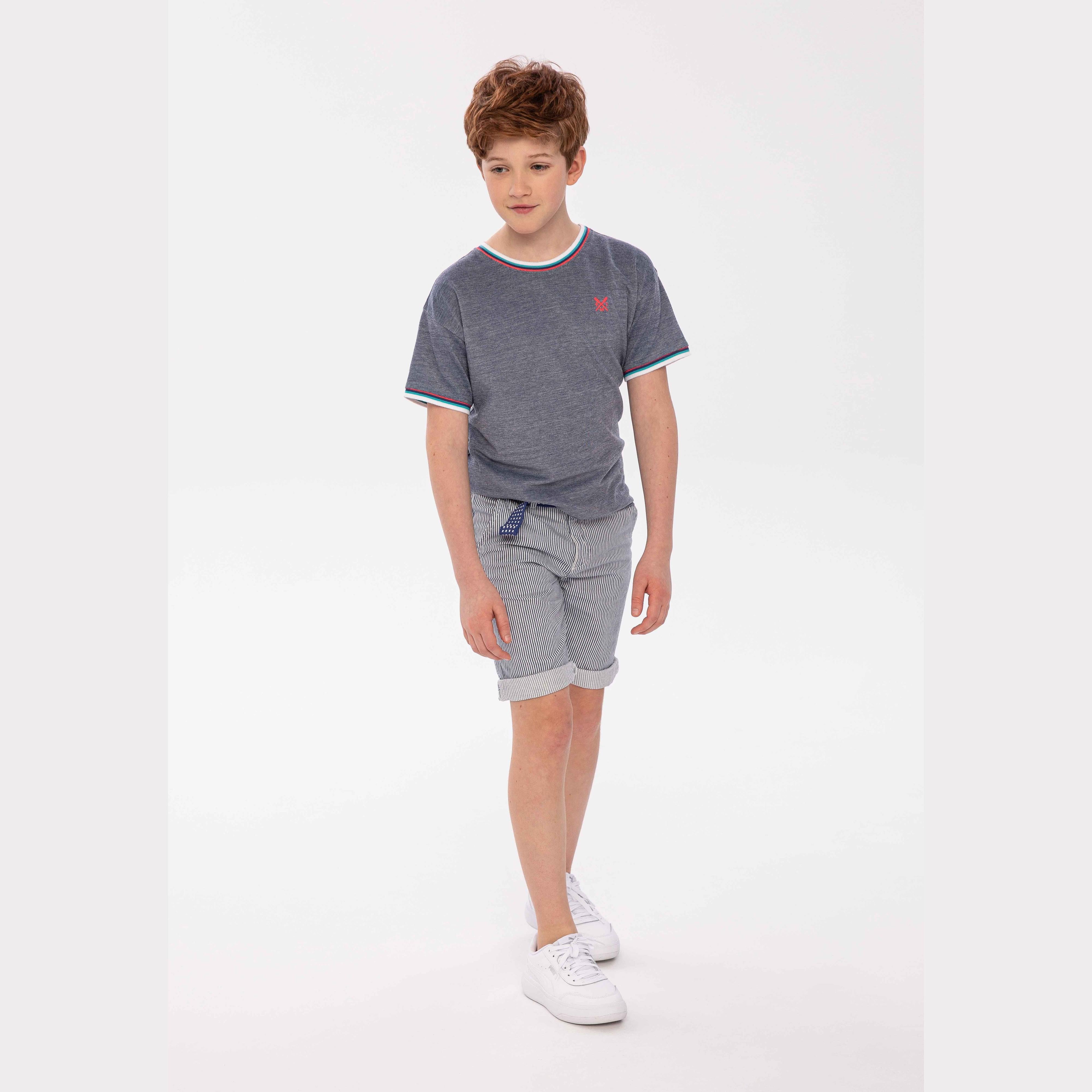 Boy wearing blue two-tone pique crew neck t-shirt with striped shorts, standing against white background