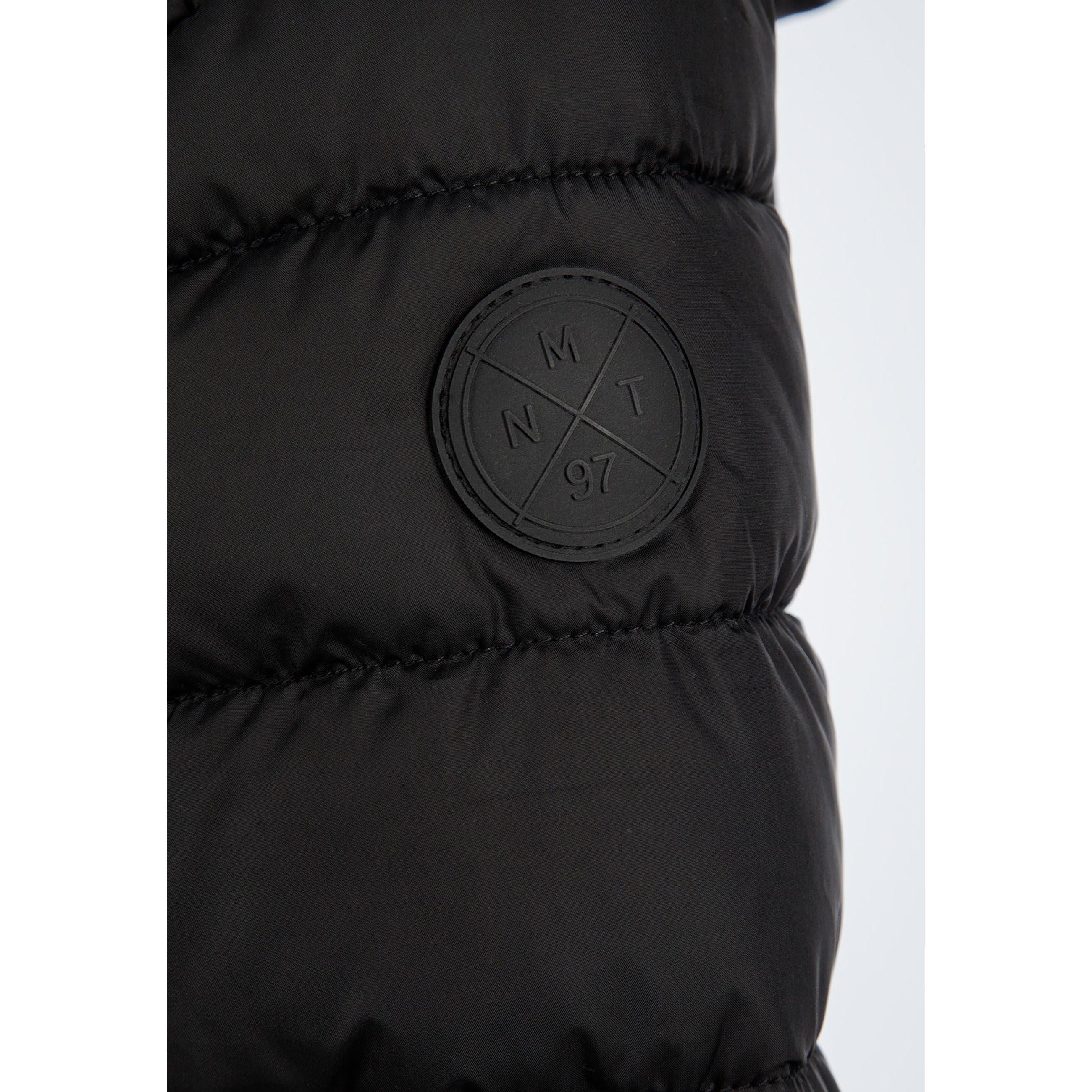 Close-up detail of black padded jacket showing quilted texture and circular Minoti logo patch on sleeve