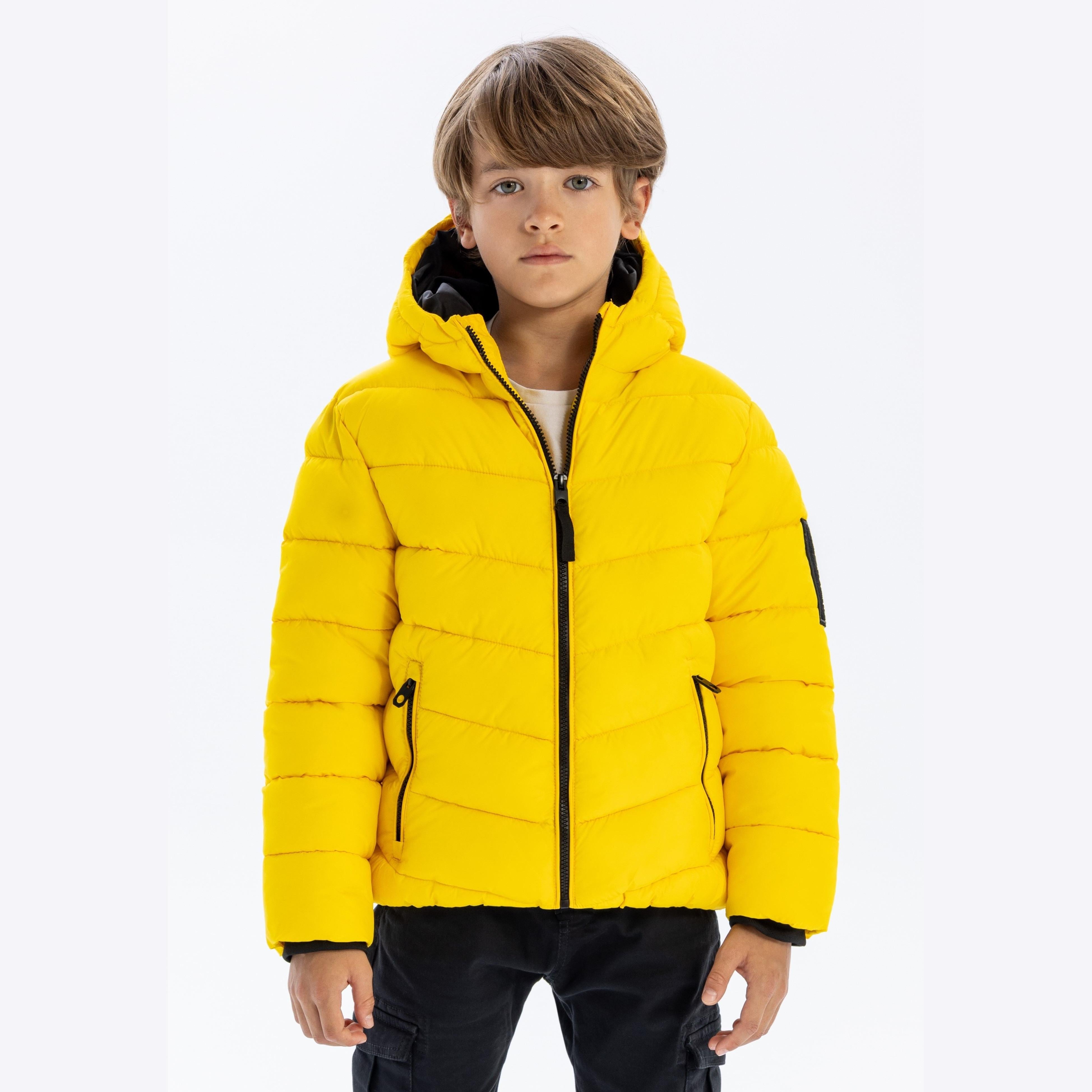 Young boy wearing bright yellow padded jacket with hood, full zip and black contrast trim, standing against light grey background