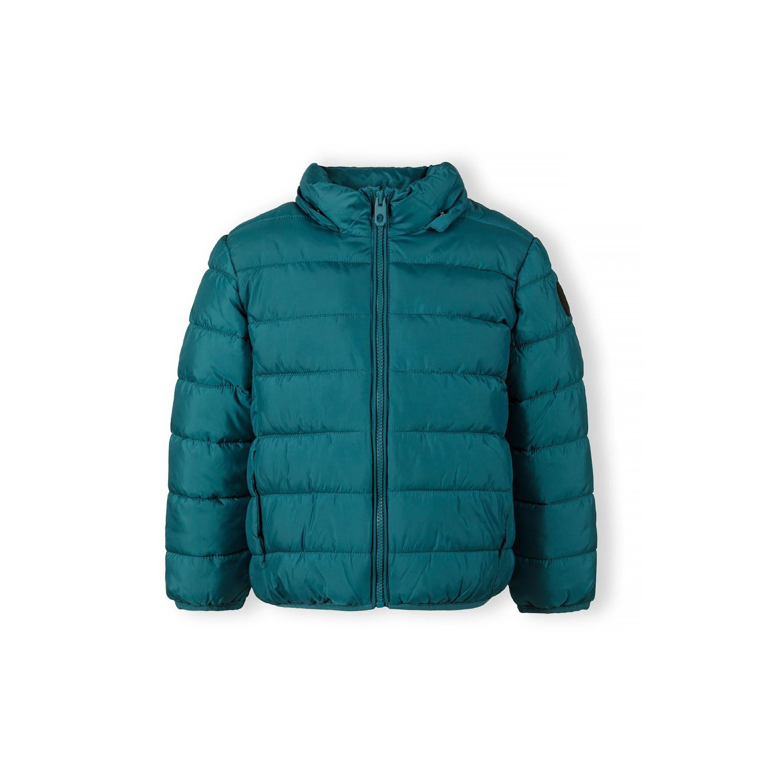 Close-up detail of turquoise padded jacket showing circular black logo patch with cross design and compass directions