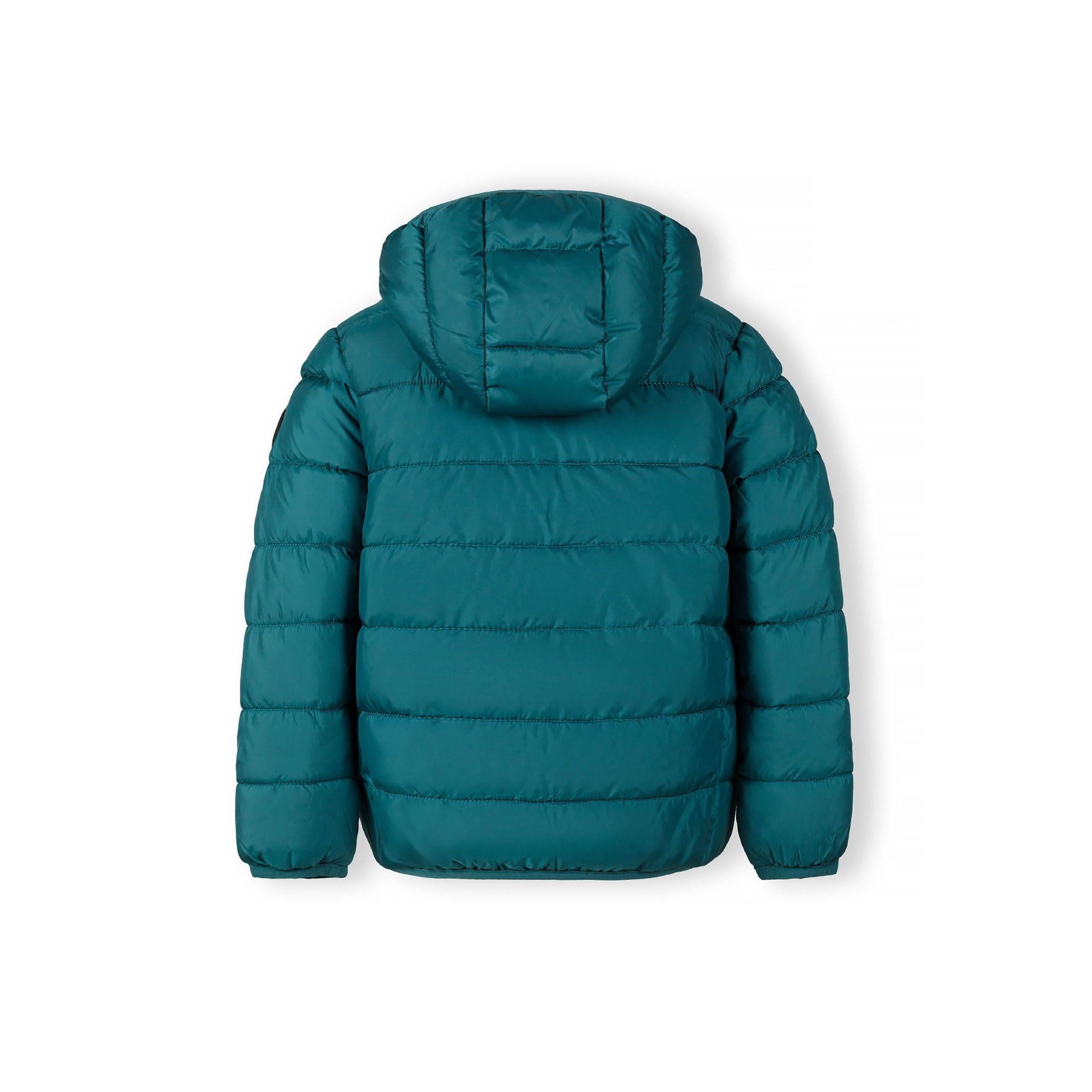 Close-up detail of turquoise padded jacket showing circular black logo patch with cross design and compass directions