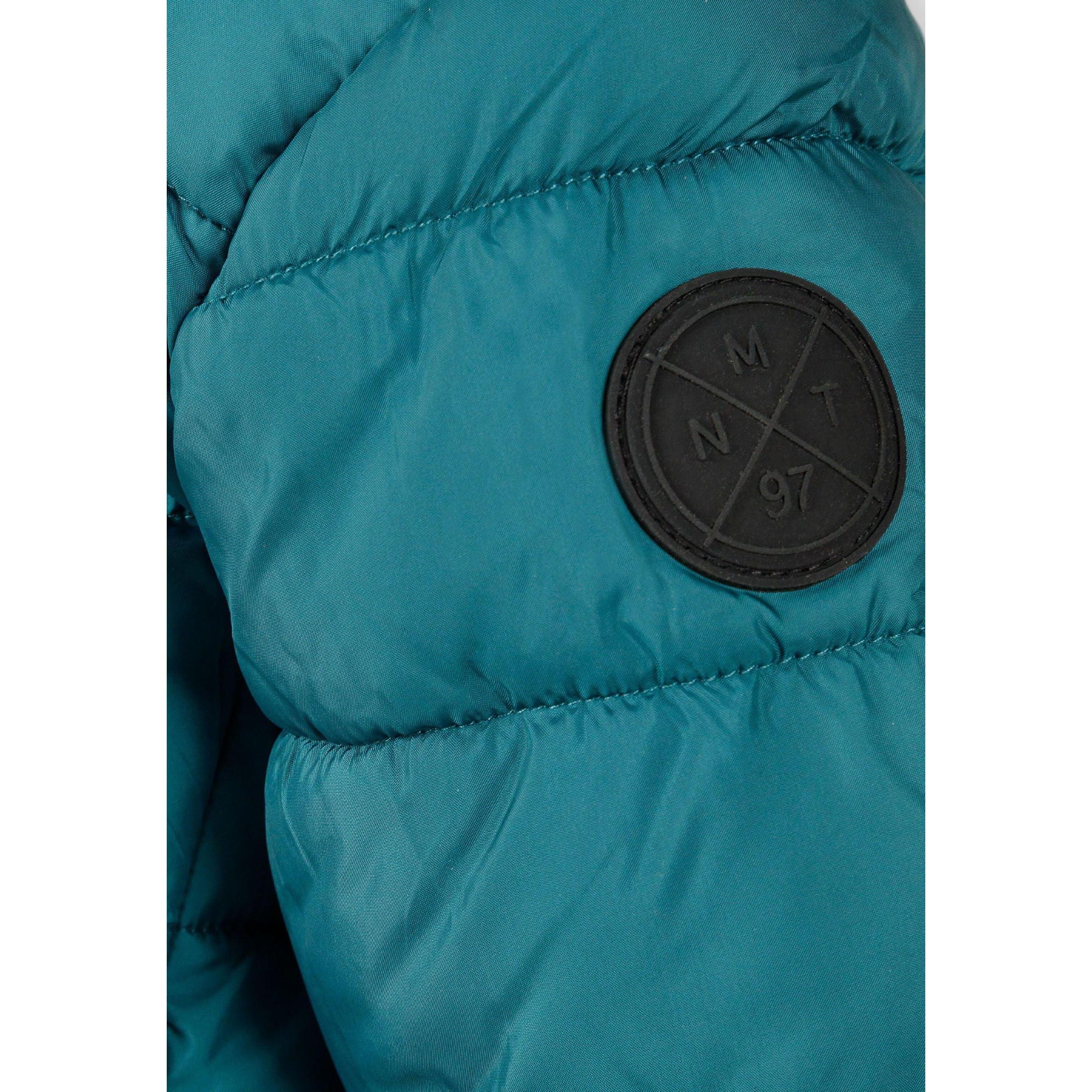 Close-up detail of turquoise padded jacket showing circular black logo patch with cross design and compass directions