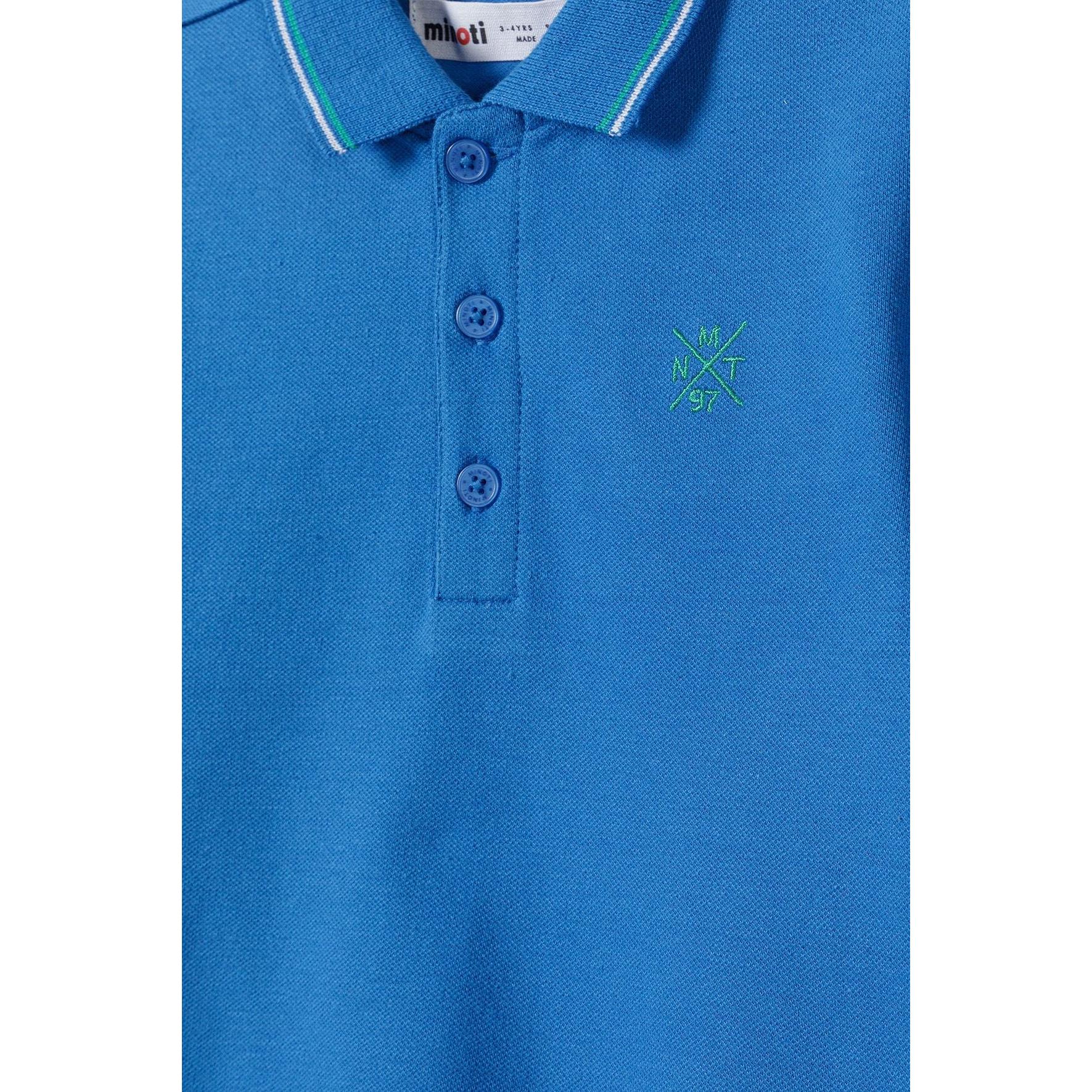 Close-up detail of blue polo shirt showing collar, button placket with blue buttons, and small green embroidered cross logo on chest
