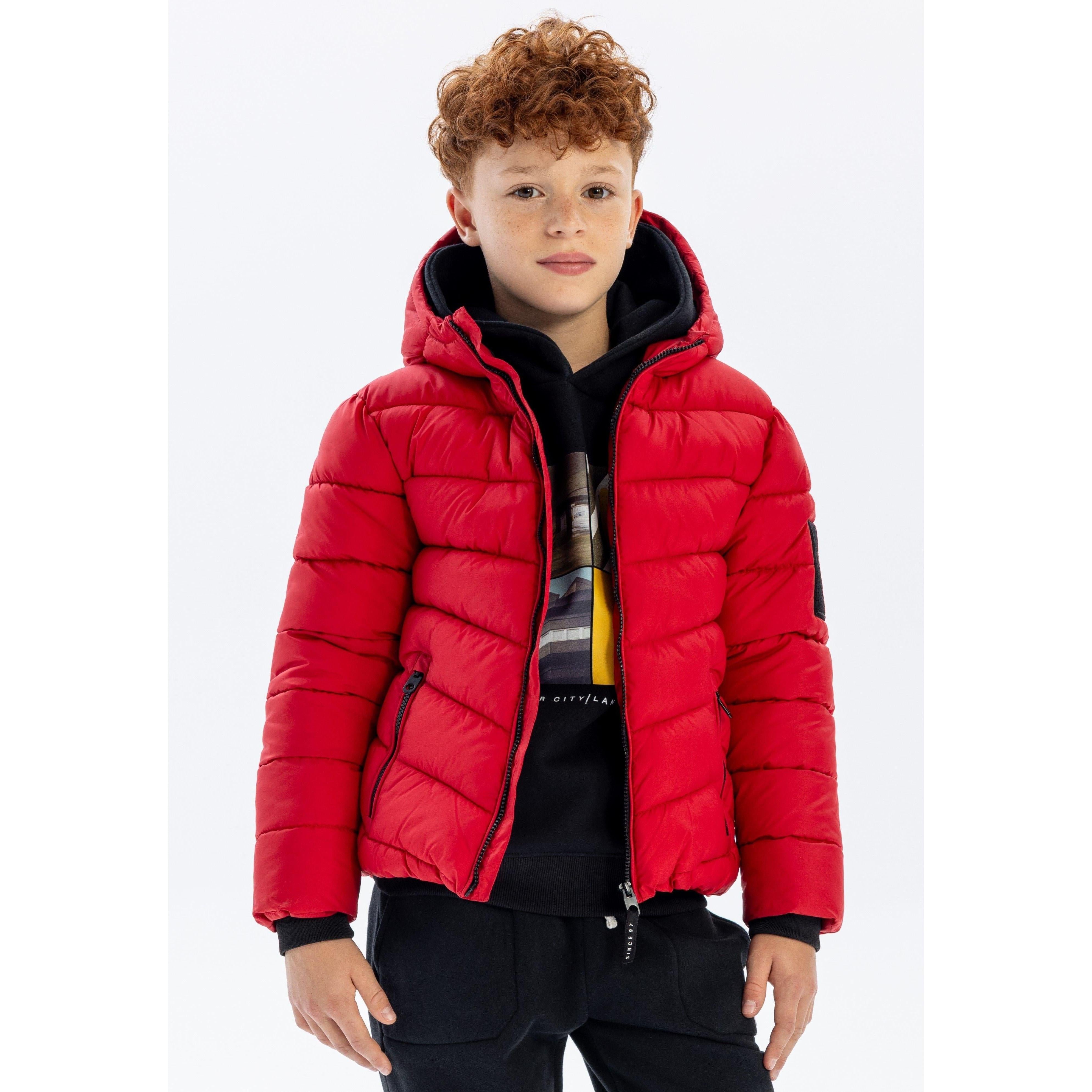 Boy wearing bright red quilted jacket with hood down, black hoodie underneath, standing against white background
