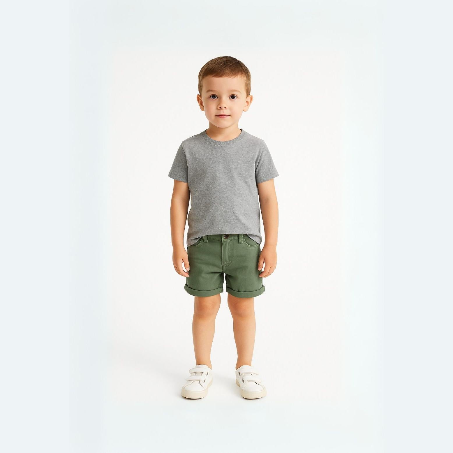 Young boy wearing grey t-shirt and khaki twill shorts with rolled hem standing against white background