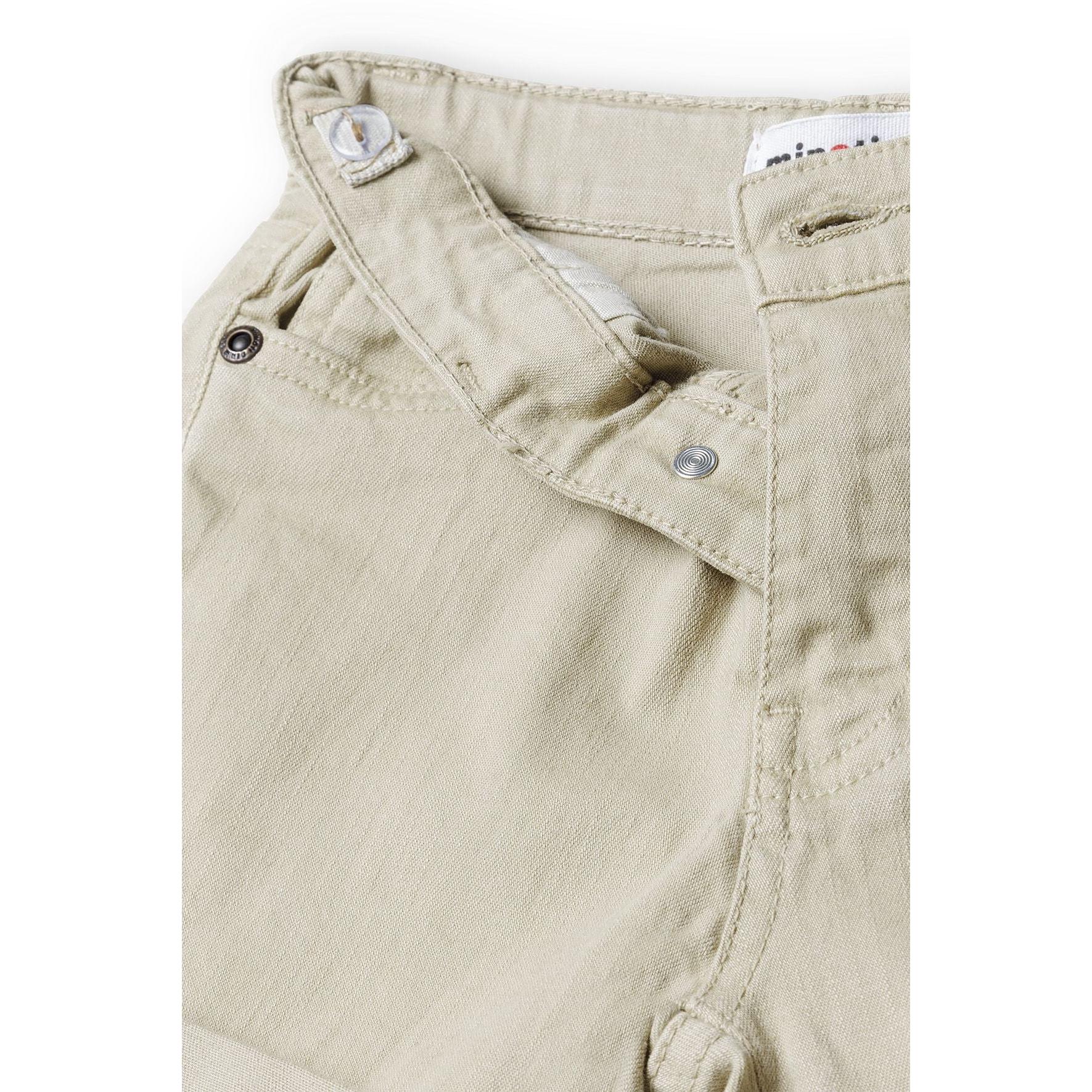 Close-up detail of beige twill shorts waistband showing button closure, zip fly and Minoti brand label