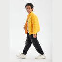 Boy wearing a bright yellow light padded jacket with a chest print, black cargo pants, and white sneakers.