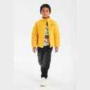 Boy wearing a bright yellow light padded jacket with a stand collar and chest print, black cargo pants, and white sneakers.