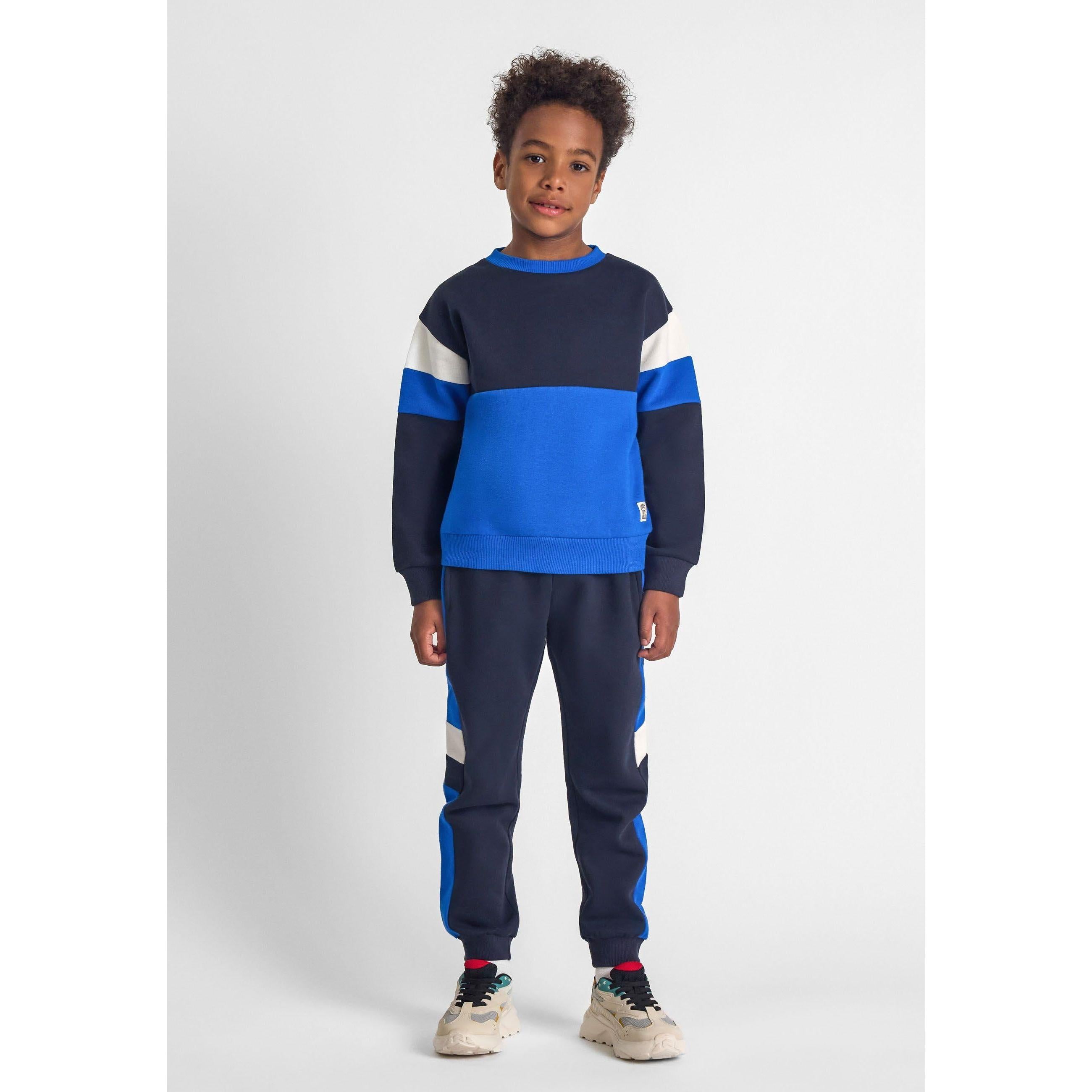 Boy wearing navy tracksuit set with blue and white colourblock panels, standing against white studio background